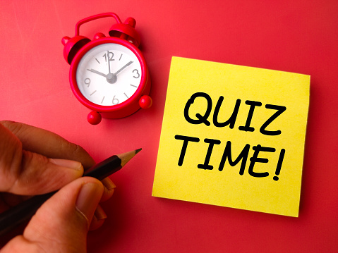Alarm clock and sticky note with the word QUIZ TIME on a red background