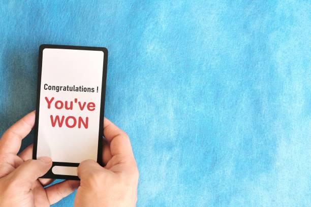 istock Winning text scam concept. Hand holding mobile phone with congratulatory message in blue background. 2074516999