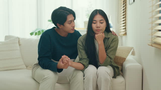 Asian sad woman crying while talking and discussing mental health problems with her husband at home. The couple communicates with each other about relationship problems with empathy.