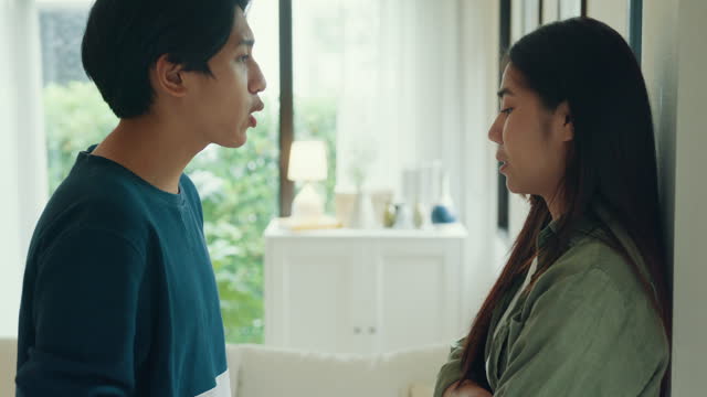 Young Asian couple angry worried quarreling arguing in living room at home. Problems in relationship.