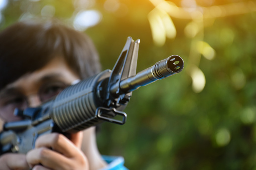 Airsoft gun or BB gun shooter holds airsoft gun and aiming it to the shooting target point ahead, soft and selective focus on the muzzle, outdoor recreational activity concept.