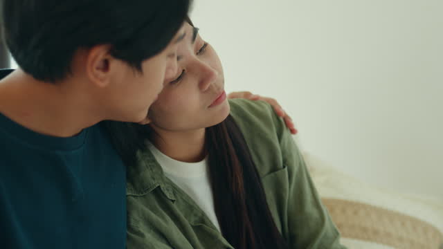 Close-up of Asian sad man crying while talking and discussing mental health problems with his wife at home. The couple communicates with each other about relationship problems with empathy.