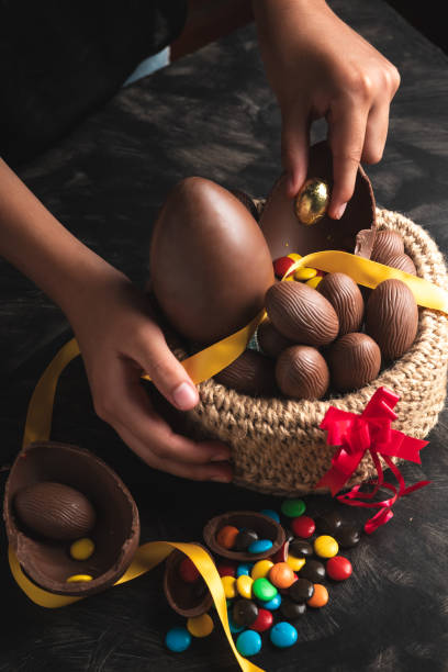 hands holding chocolate easter eggs from a basket basket of chocolate Easter eggs, large and small with sprinkles chocolate fingers stock pictures, royalty-free photos & images