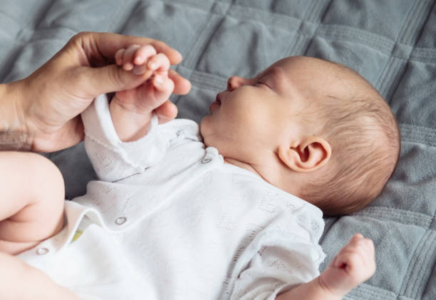 The baby lies on the blanket, the mother holds his hands stock photo
