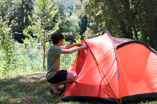 Young man preparing his tent and sleeping bag at a Patagonian campsite surrounded by forests, rivers and mountains during his summer vacation in Argentina.