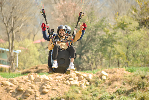 Paraglider instructor with tourist man comes down to landing in mountains of Himachal Pradesh, Bir- Billing India.