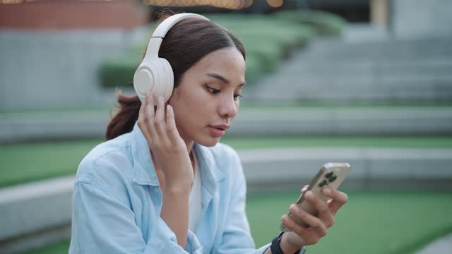 An Asian woman turns on music on her smartphone and listens with wireless headphones