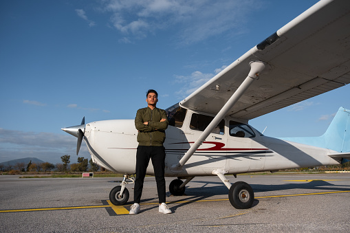 Young pilot candidate taking flight training looks at camera in front of retro airplane