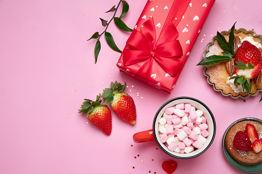 Festive pink background with cupcake, strawberries, chocolates, hot drink. Birthday celebration. Top view, copy space