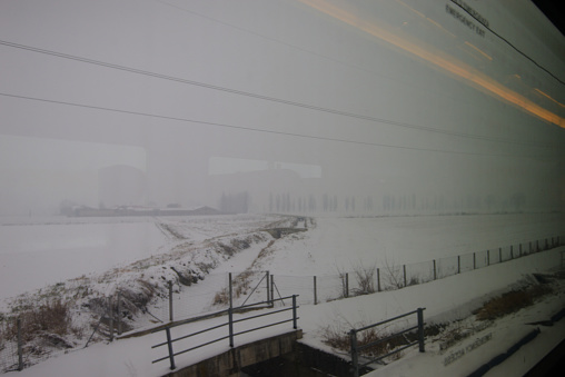 Gloomy snowy fields in rural Italy photographed from the train at the end of the February 2018 cold snap, with reflections on the train window making a counterpoint with lines in the landscape and a sense of movement.