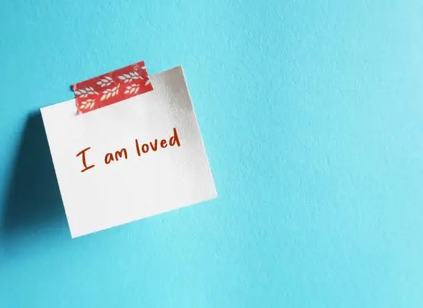 Stick note on blue copy space background with handwritten message - I am loved - positive self-loved affirmation to boost self esteem -  to accept you are worthy of love and respect