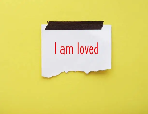 Stick note on yellow background with handwritten message - I am loved - positive self-loved affirmation to boost self esteem -  to accept you are worthy of love and respect