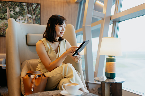 An Asian Chinese businesswoman using digital tablet while waiting for flight at airport lounge. Business travel concept.