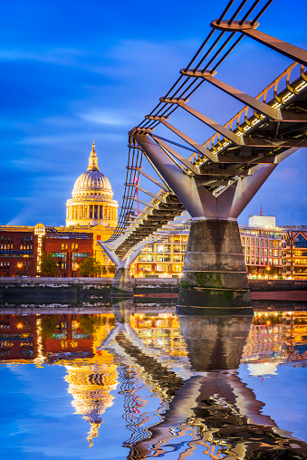 London, United Kingdom. St Paul's Anglican cathedral dome and Millennium Bridge, early in the evening twilight Thames River water reflection.