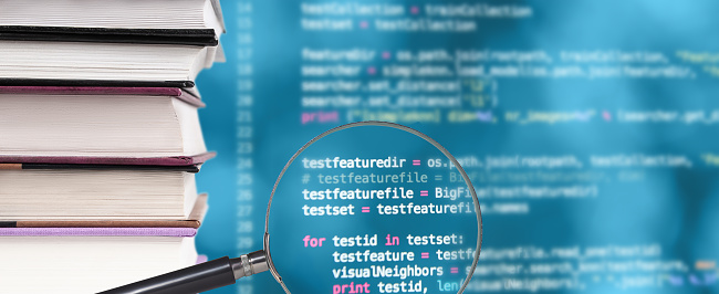 Stack of books, source code and magnifying glass on a blurred background