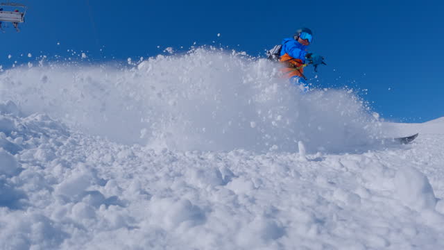 Slow Motion: Skier descends ski slope and sprays snow at camera