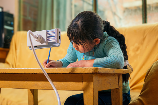 underprivileged latina girl doing school homework with a cell phone - education concept