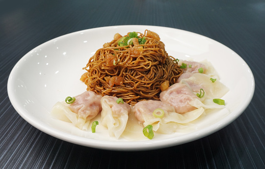 stir fried dry wanton noodle mee in dark soy sauce with meat dumpling in plate on dark grey wood table asian dim sum halal food restaurant cuisine banquet menu for cafe