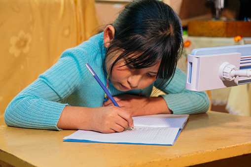 latina girl copying homework from cell phone to notebook - education concept