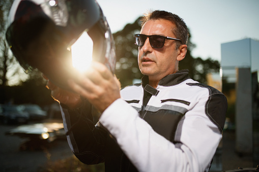 Portrait of mature man wearing moto jacket and sunglasses, putting cycling helmet on, enjoying life and freedom