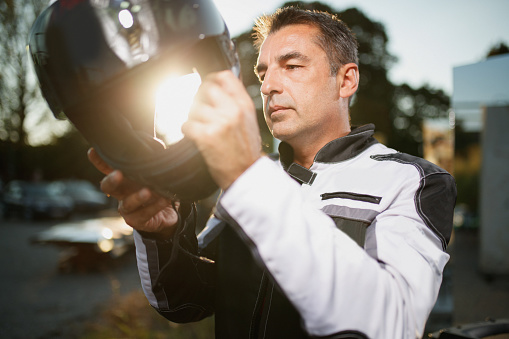 Portrait of mature man in moto jacket putting cycling helmet on, enjoying life and freedom