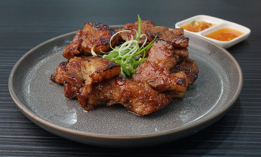 Thai bbq grilled tender pork chop meat with sauce in plate on dark grey wood table asian dim sum halal food restaurant cuisine banquet menu for cafe
