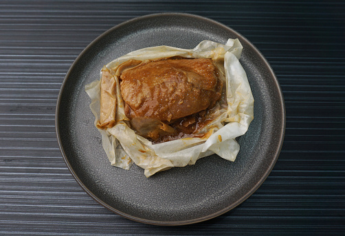 chinese baked handmade paper wrapped chicken meat with herbal dark soy sauce in plate on dark grey wood table asian dim sum halal food restaurant cuisine banquet menu for cafe