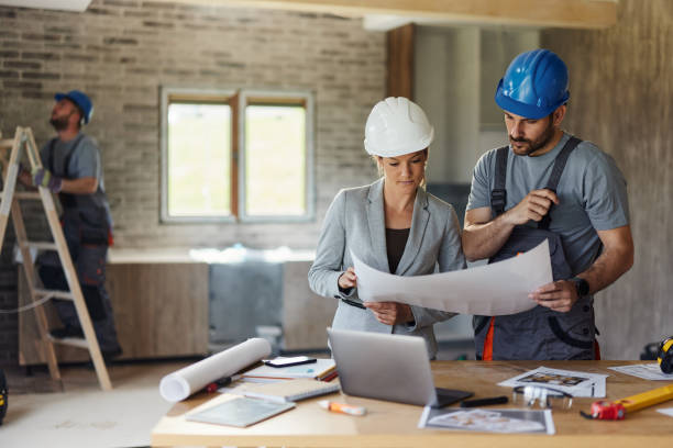 Female inspector and manual worker reading plans at renovating home.