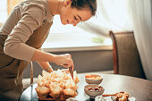 young woman applies cream to cupcakes in craft paper. the concept of food delivery. a birthday package. small business. bakery chef bakes cakes in kitchen