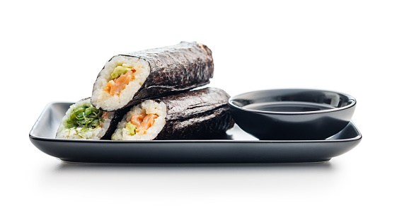 A sushi roll with rice, seaweed, and various fillings neatly placed on a black plate, accompanied by a bowl of soy sauce.