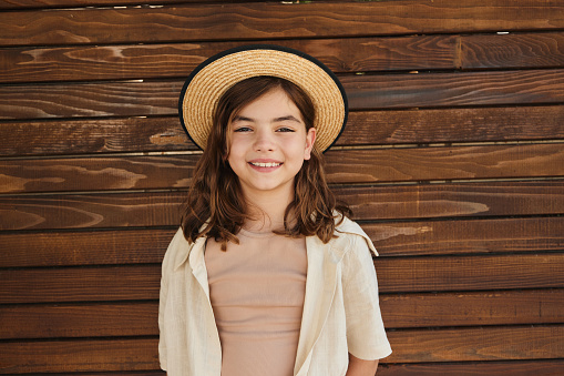 Portrait of happy girl with a hat standing against brown background and looking at camera. Copy space.