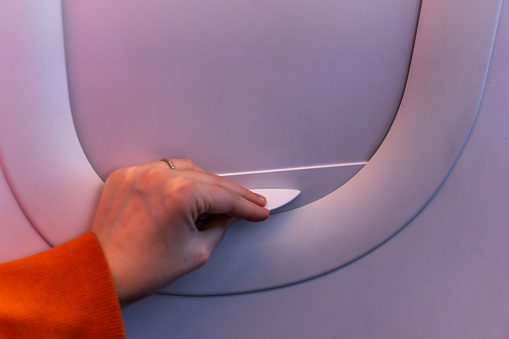 Woman's hand closing the airplane window blind.