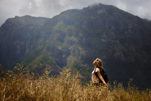 Smiling female backpacker enjoying while standing in tall grass with her arms outstretched and eyes closed on a mountain. Copy space.