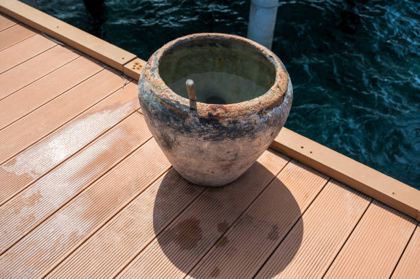 Brown round water container. On a wooden bridge under which is blue water.