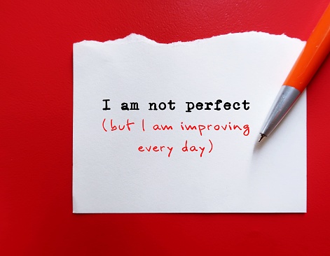 On red background - pen wrote on paper - I am not perfect but I am improving everyday - concept of positive self-talk to accepta flaws and imperfections and boost self-respect