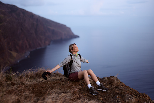 Smiling female backpacker relaxing with outstretched arms from her hike on a mountain above the sea. Copy space.