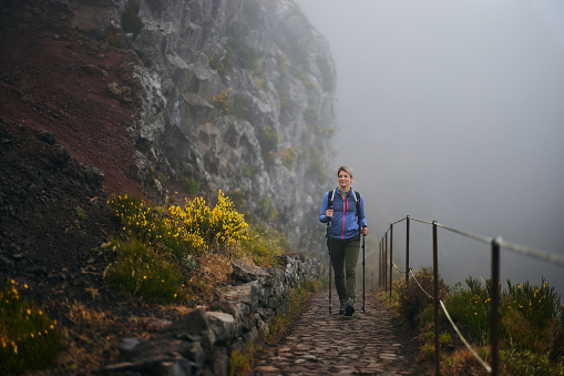 Smiling female backpacker hiking on a path during foggy day on a mountain. Copy space.