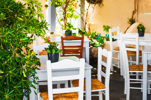 National greek cafe in Santorini island, Greece. Tavern with white wooden tables and chairs on the terrace with green trees