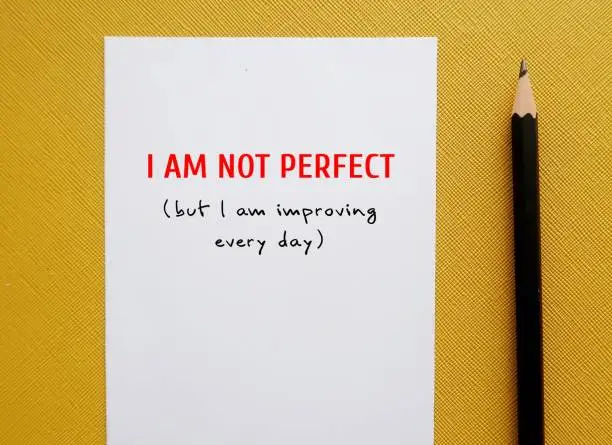On yellow background - pen wrote on paper - I am not perfect but I am improving everyday - concept of positive self-talk to accept flaws and imperfections and boost self-respect