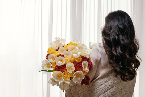 Beautiful curly woman with spring flowers tulips in hands. Women's Day. copy space