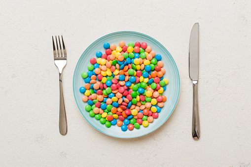 cutlery on table and sweet plate of candy. Health and obesity concept, top view on colored background.