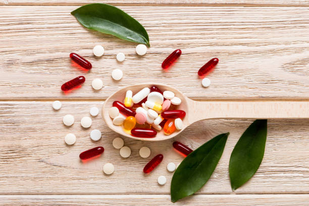 vitamin capsules in a spoon on a colored background. pills served as a healthy meal. red soft gel vitamin supplement capsules on spoon - fish oil cooking oil capsule herbal medicine stock-fotos und bilder
