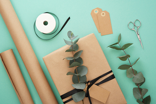 Summer gift wrapping. Brown craft wrapping paper, black ribbon, scissors, eucalyptus, tags. Mint background.