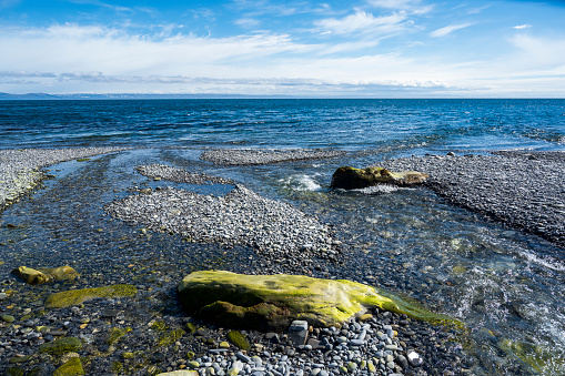 Stream flows into sea on stone beach