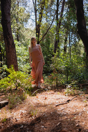 Beautiful blond woman wearing terracotta sleeveless dress wandering alone in the woods on the coast, enjoying time by herself