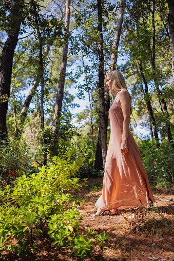 Beautiful blond woman wearing terracotta sleeveless dress wandering alone in the forest on the coast, enjoying time on her own