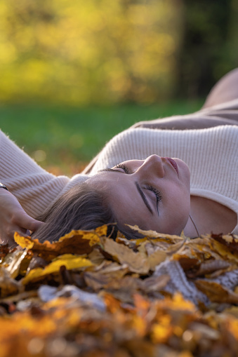 Autumn Walk. Female portrait. A happy girl lies with her eyes closed on the ground in a park among yellow leaves; side view, rear view