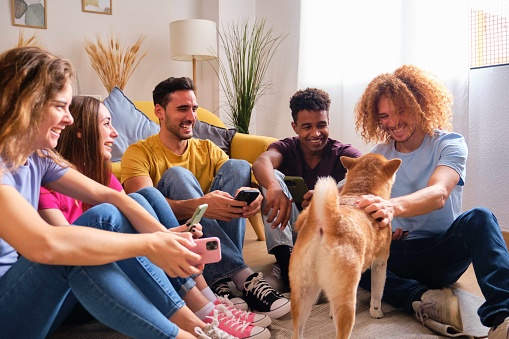 Happy group of students in a shared flat with their Shiba Inu dog sitting on the floor.