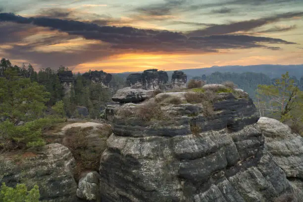 Rugged rocks at Basteibridge at sunset. Wide view over trees and mountains. National park in Germany