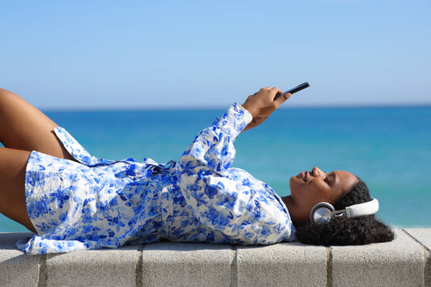Happy black woman watching media lying on the beach